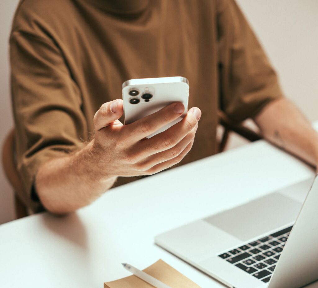 Person interacting with smartphone at tidy desk with laptop and coffee mug, showcasing modern technology.